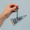 Hand holding a small pennant with 'GO PHILS' text against a light blue background