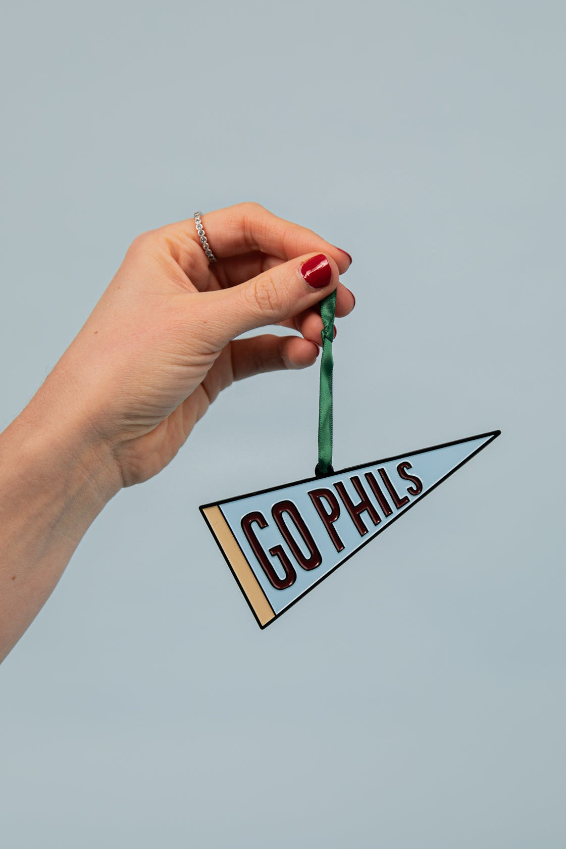 Hand holding a small pennant with 'GO PHILS' text against a light blue background